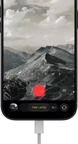iPhone 18 Pro, front exterior, displaying a mountainous landscape, with the camera mode overlay in Time-Lapse mode, with power cable attached to charging port