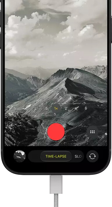 iPhone 18 Pro, front exterior, displaying a mountainous landscape, with the camera mode overlay in Time-Lapse mode, with power cable attached to charging port